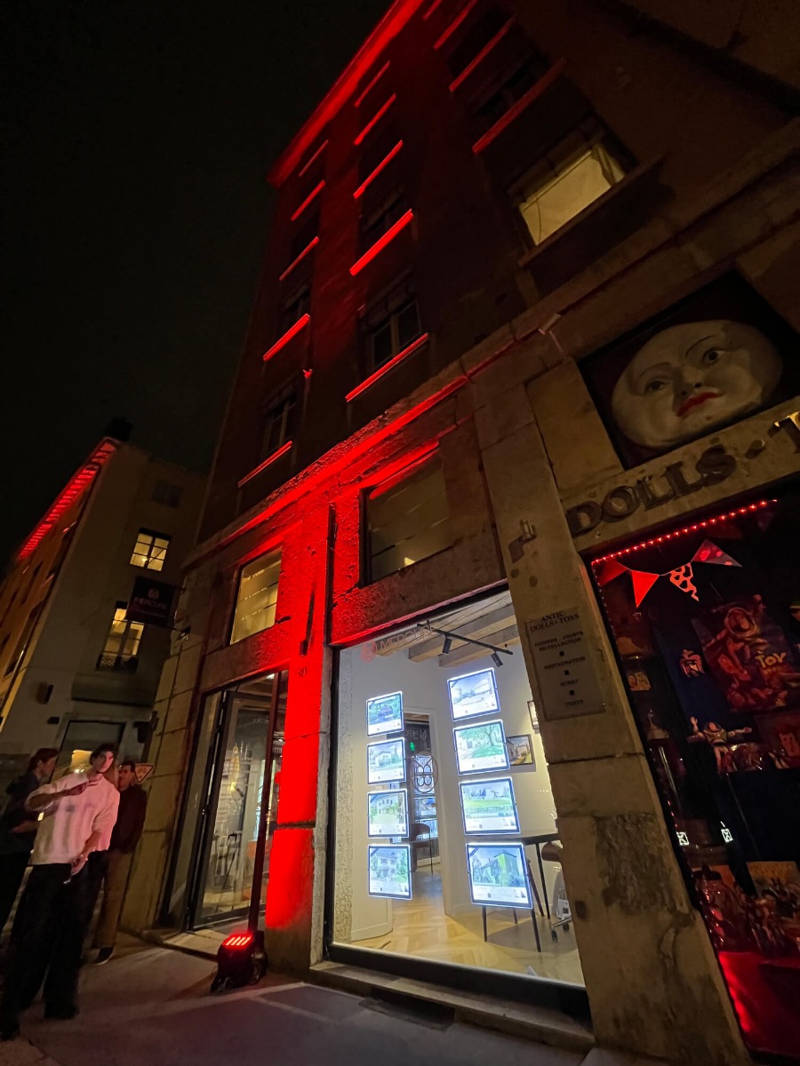 Devanture d'un magasin d'immobilier avec la façade de l'imeumble illuminés en rouge