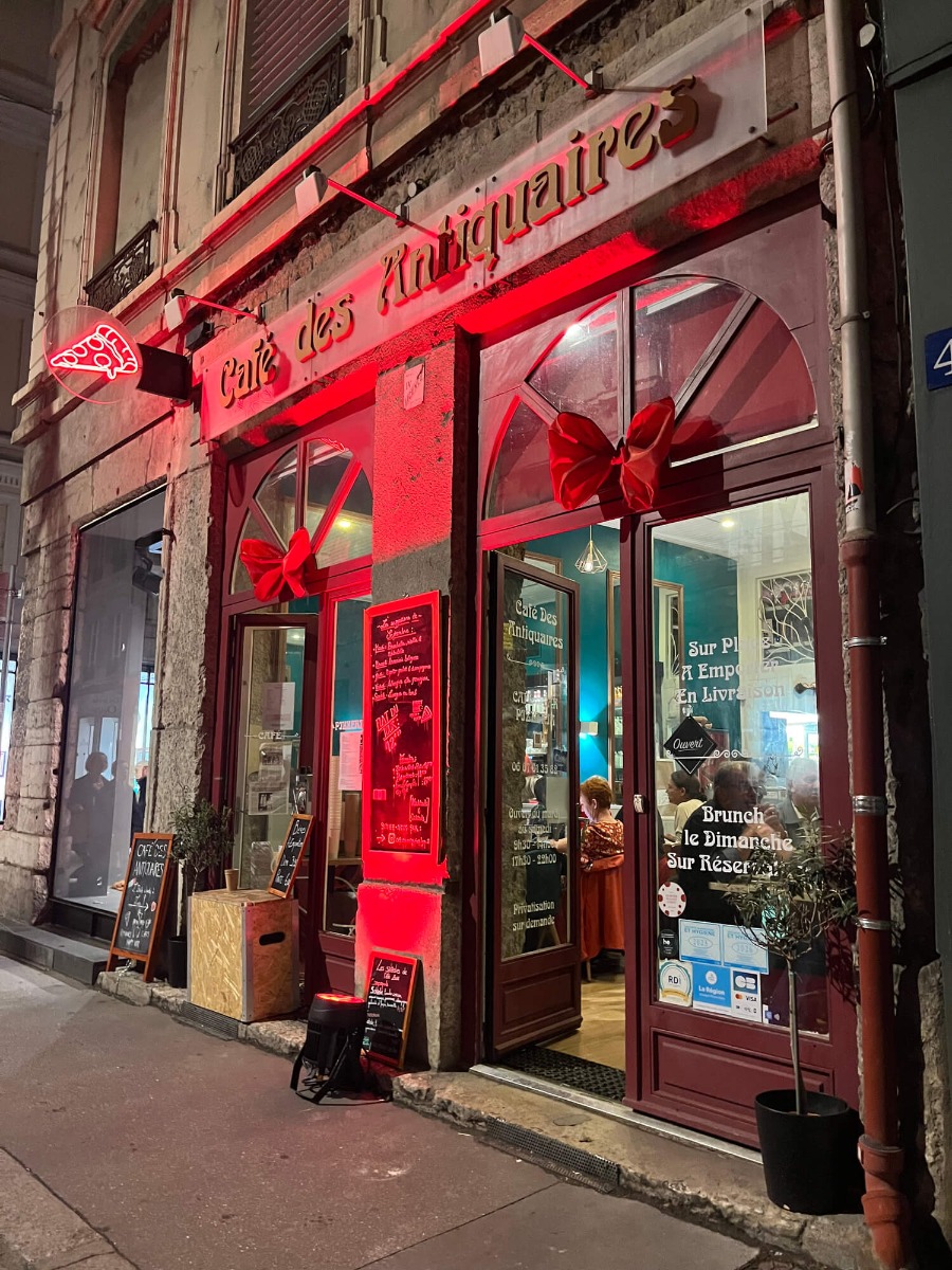 Devanture de café éclairée en rouge en lumière rasante, projecteur LED posé sur le trottoir au pied de la façade